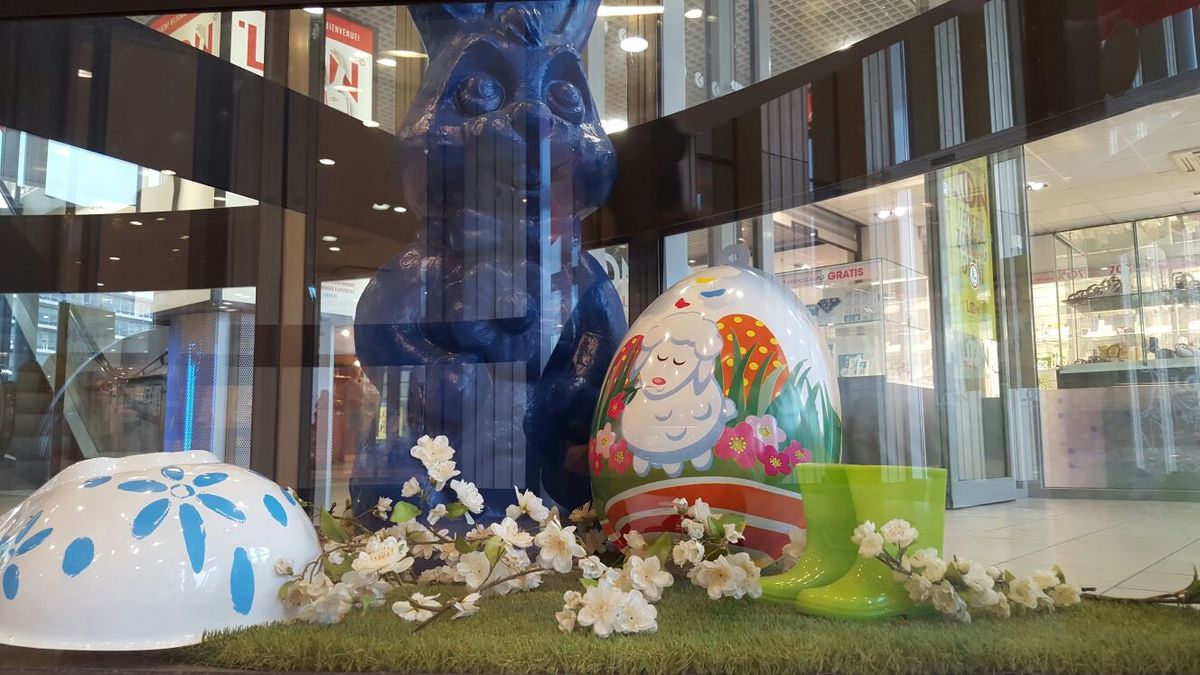 Osterdekoration mit großem Osterhasen, bemaltem Osterei, Blütenzweigen und grünen Gummistiefeln in einem Einkaufszentrum