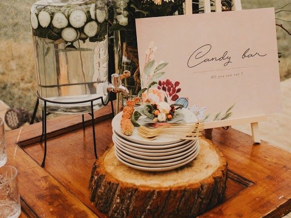 Tischstyling mit Getränkespender, Tellern auf Holzscheibe und Candy-Bar-Schild