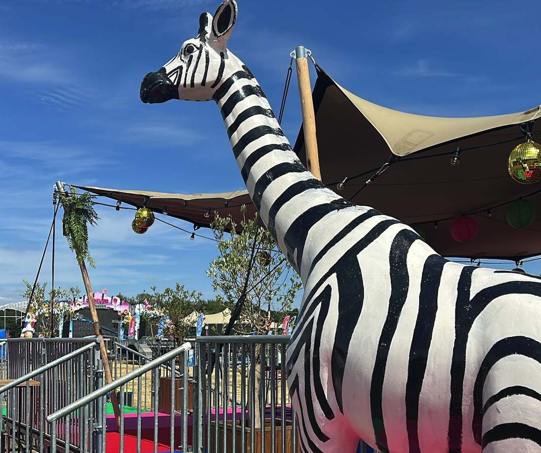 Zebra-gestreifte Giraffe als Eyecatcher auf einem bunten Festivalgelände