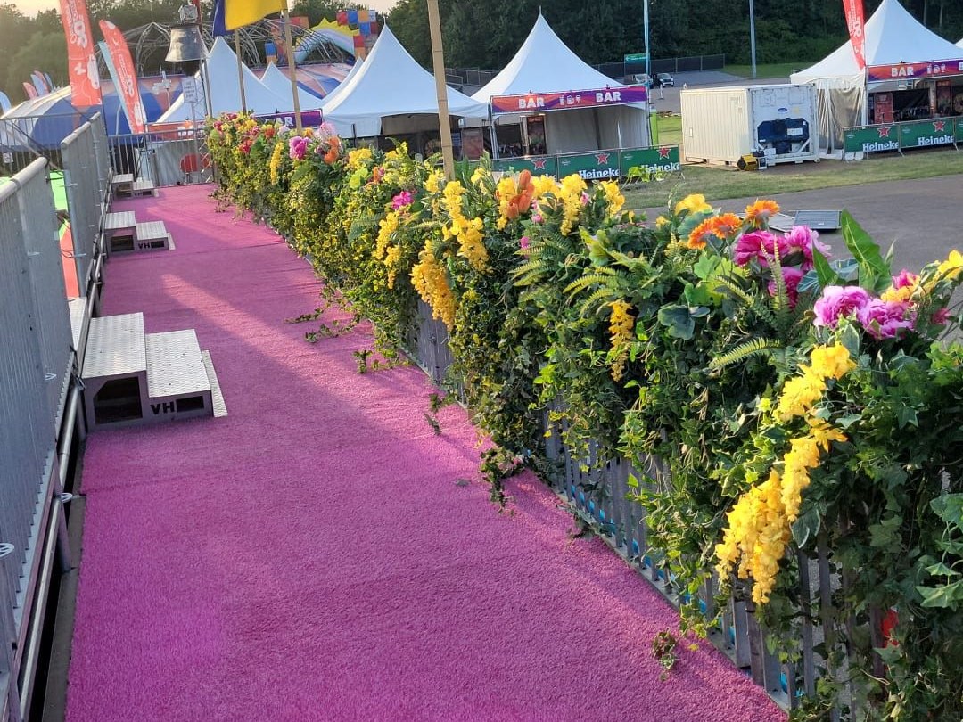Blumenwand mit gelben und rosa Blumen entlang eines rosa Teppichs auf einem Festivalgelände
